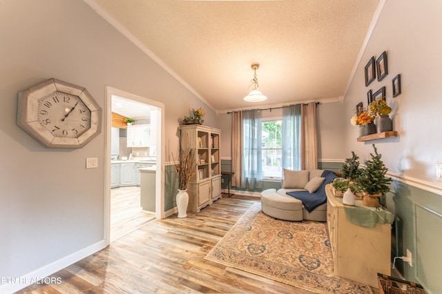 living area featuring a textured ceiling, light hardwood / wood-style flooring, ornamental molding, and vaulted ceiling