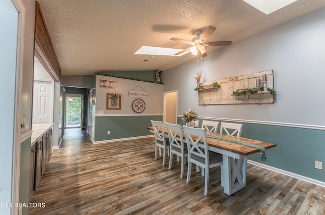 dining area with a textured ceiling, dark wood-type flooring, lofted ceiling with skylight, and ceiling fan