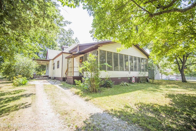 view of front of home with an attached carport, a sunroom, driveway, and a front lawn