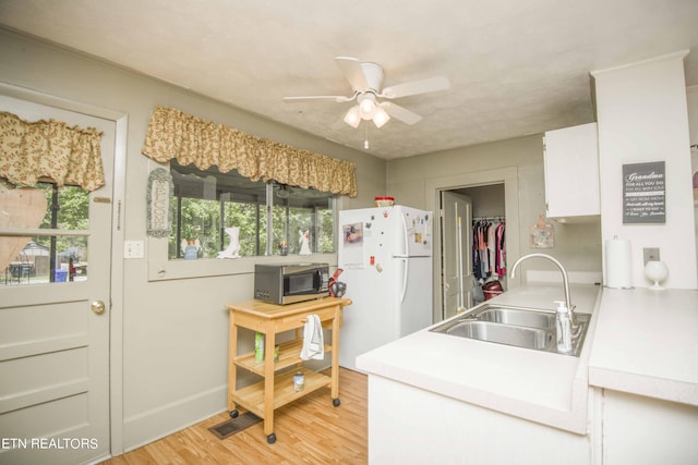 kitchen featuring stainless steel microwave, freestanding refrigerator, light countertops, light wood-type flooring, and a sink