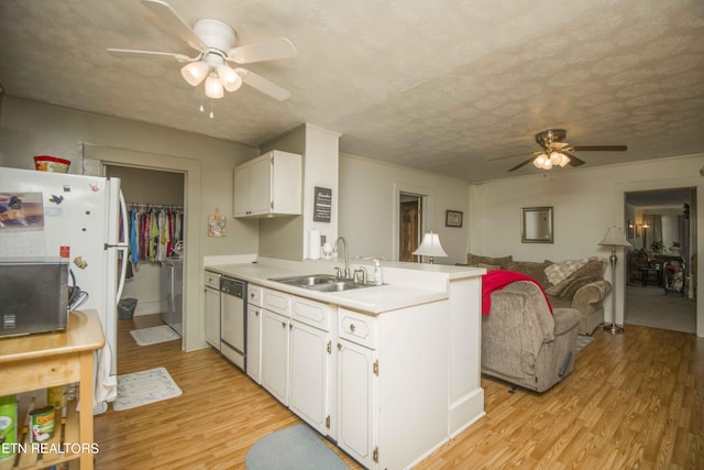 kitchen with light wood finished floors, stainless steel dishwasher, white cabinetry, a sink, and a peninsula