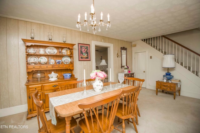 carpeted dining space featuring crown molding, an inviting chandelier, and wooden walls