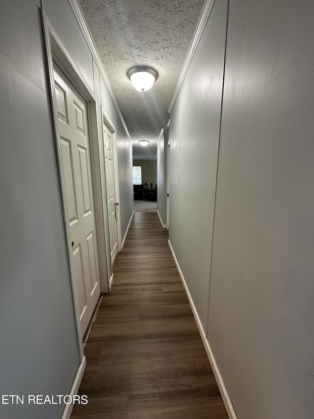 hall with dark wood-style floors, ornamental molding, a textured ceiling, and baseboards