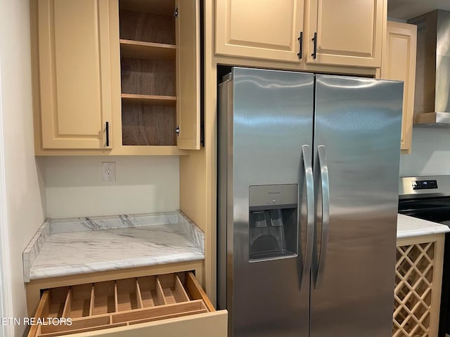 kitchen with cream cabinetry, stainless steel fridge, stove, and wall chimney range hood