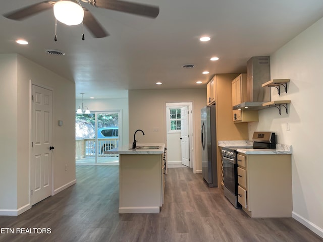 kitchen with ceiling fan with notable chandelier, wall chimney range hood, sink, dark hardwood / wood-style flooring, and stainless steel appliances