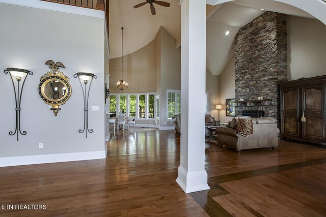 interior space featuring ceiling fan with notable chandelier, a fireplace, high vaulted ceiling, and dark wood-type flooring