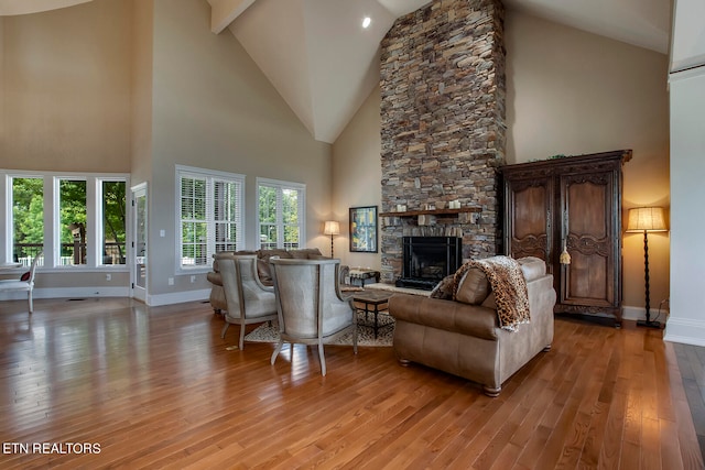 living room with high vaulted ceiling, light hardwood / wood-style floors, and a stone fireplace