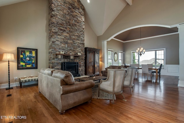 living room with hardwood / wood-style flooring, a fireplace, an inviting chandelier, high vaulted ceiling, and ornamental molding