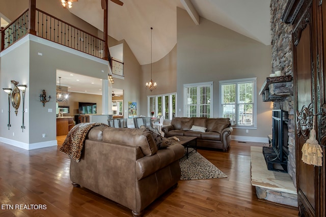 living room with ceiling fan with notable chandelier, high vaulted ceiling, dark hardwood / wood-style flooring, and a stone fireplace