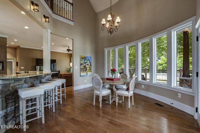 dining area featuring ceiling fan with notable chandelier, dark hardwood / wood-style flooring, plenty of natural light, and a towering ceiling