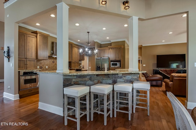 kitchen with a kitchen breakfast bar, dark hardwood / wood-style flooring, light stone countertops, appliances with stainless steel finishes, and ornate columns