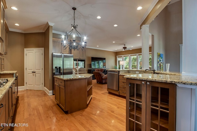 kitchen with decorative light fixtures, ceiling fan with notable chandelier, light stone counters, light hardwood / wood-style floors, and an island with sink