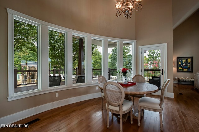 dining space featuring dark wood-type flooring, an inviting chandelier, and a towering ceiling