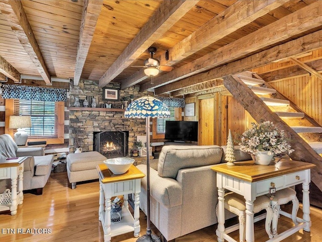 living room with light wood-type flooring, ceiling fan, beam ceiling, and a stone fireplace