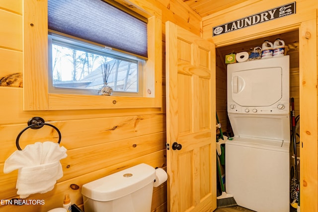 bathroom featuring toilet, wooden walls, and stacked washer / drying machine