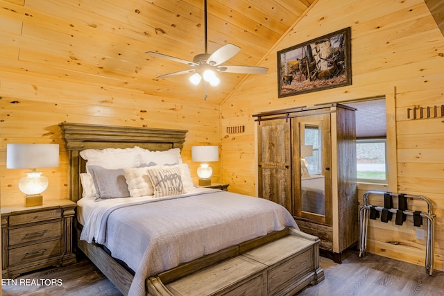 bedroom featuring vaulted ceiling, dark hardwood / wood-style floors, a barn door, ceiling fan, and wooden walls