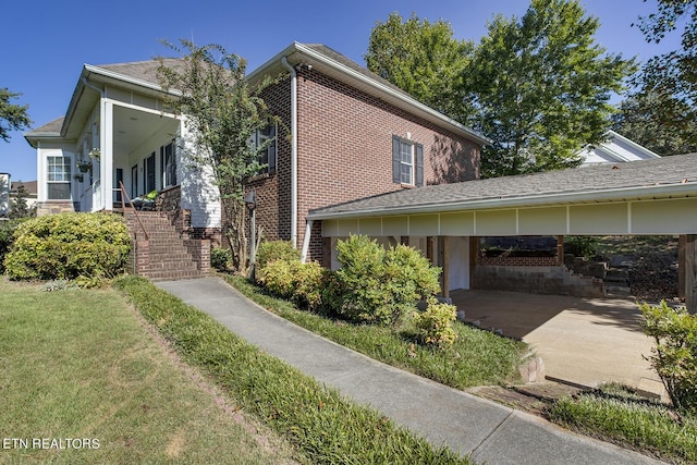 view of side of property with brick siding, a lawn, and stairs