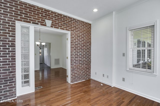 unfurnished room with brick wall, wood finished floors, visible vents, and an inviting chandelier