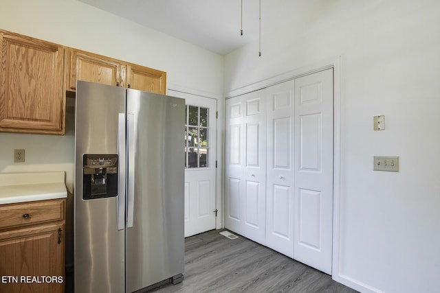 kitchen with brown cabinetry, light countertops, light wood-style flooring, and stainless steel fridge with ice dispenser