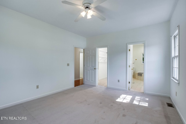 unfurnished bedroom with a walk in closet, a closet, connected bathroom, light colored carpet, and ceiling fan