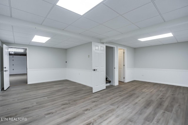 finished below grade area featuring stairs, a paneled ceiling, a wainscoted wall, and wood finished floors