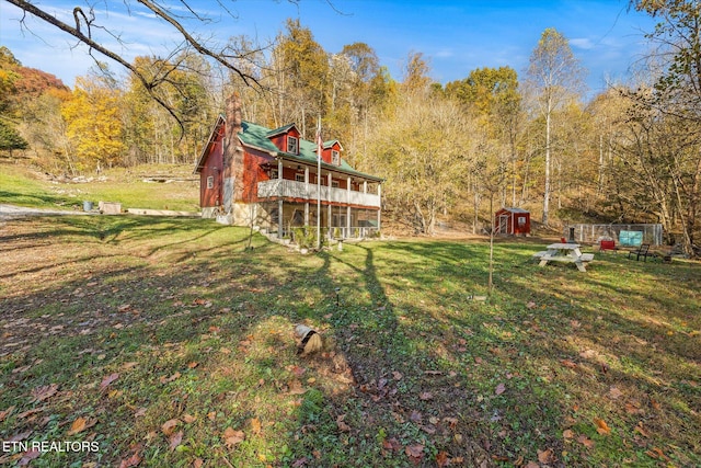 rear view of property with a shed, a lawn, and a balcony