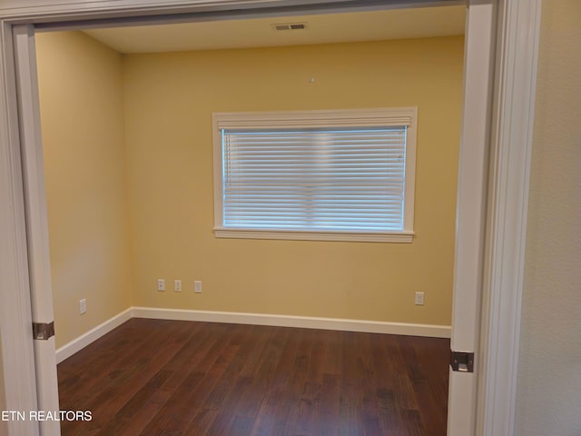 spare room with baseboards, visible vents, and dark wood-style flooring