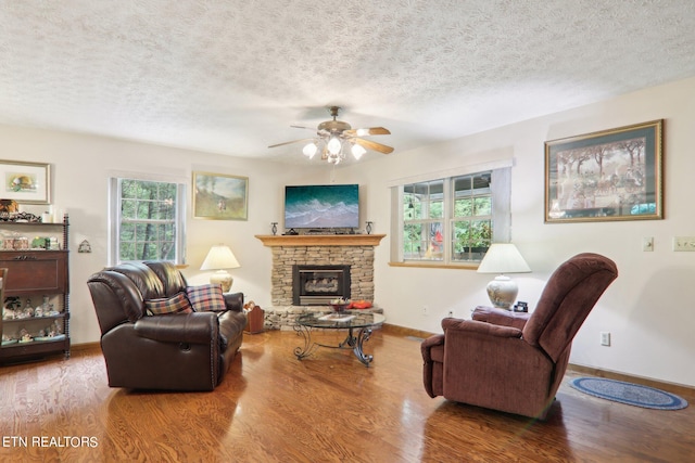 living room with ceiling fan, hardwood / wood-style flooring, a textured ceiling, and a stone fireplace