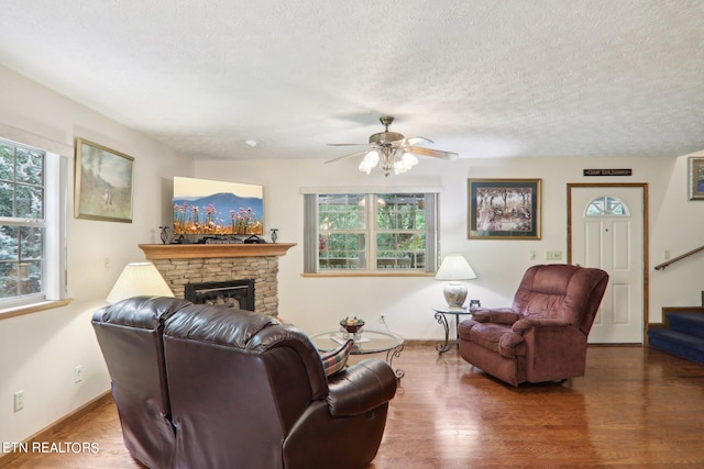 living room with a textured ceiling, ceiling fan, dark hardwood / wood-style flooring, and a fireplace