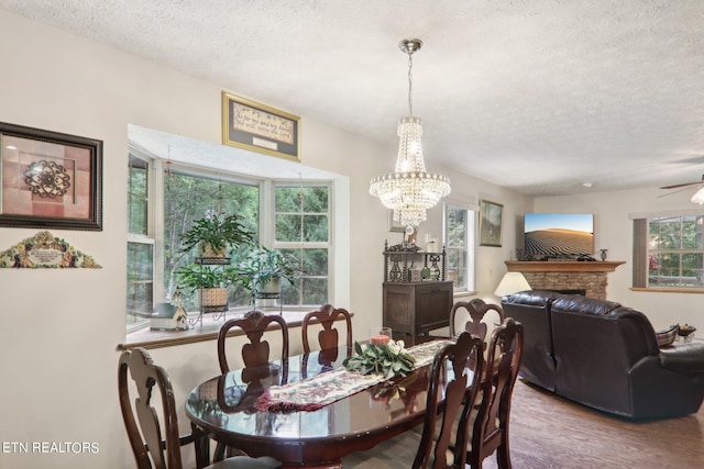 dining area featuring a textured ceiling, ceiling fan with notable chandelier, hardwood / wood-style flooring, and a fireplace