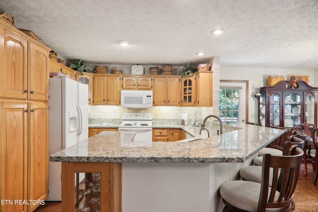 kitchen with light stone countertops, white appliances, kitchen peninsula, sink, and decorative backsplash