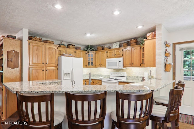 kitchen with hardwood / wood-style flooring, white appliances, light stone countertops, kitchen peninsula, and a textured ceiling