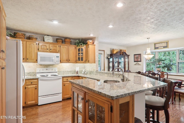 kitchen with light hardwood / wood-style flooring, decorative light fixtures, white appliances, sink, and kitchen peninsula