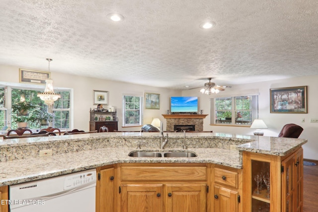 kitchen featuring dishwasher, a fireplace, ceiling fan with notable chandelier, sink, and a textured ceiling