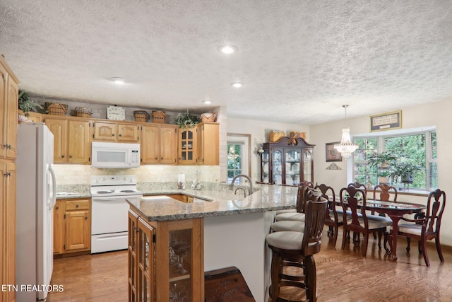 kitchen with light stone countertops, white appliances, pendant lighting, light hardwood / wood-style floors, and kitchen peninsula