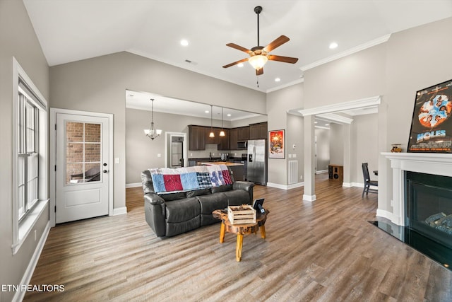 living room with ceiling fan with notable chandelier, crown molding, lofted ceiling, and light hardwood / wood-style floors