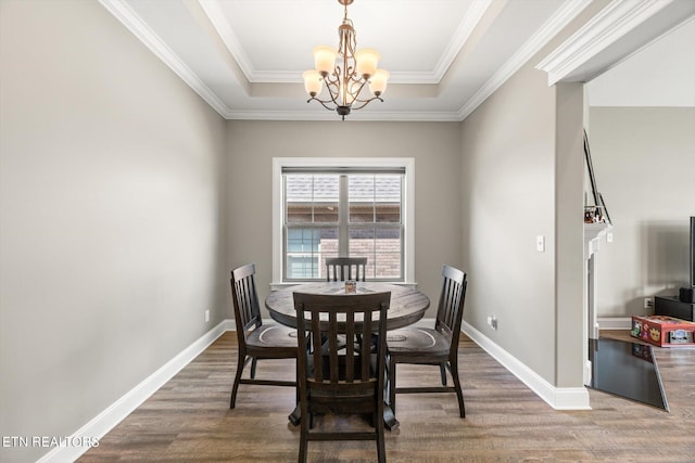 dining space with ornamental molding, an inviting chandelier, wood-type flooring, and a tray ceiling