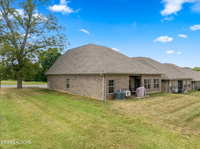 rear view of house featuring central air condition unit, roof with shingles, brick siding, and a yard