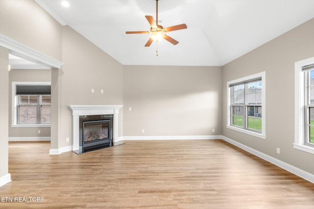 unfurnished living room with vaulted ceiling, a fireplace with flush hearth, baseboards, ceiling fan, and light wood-style flooring