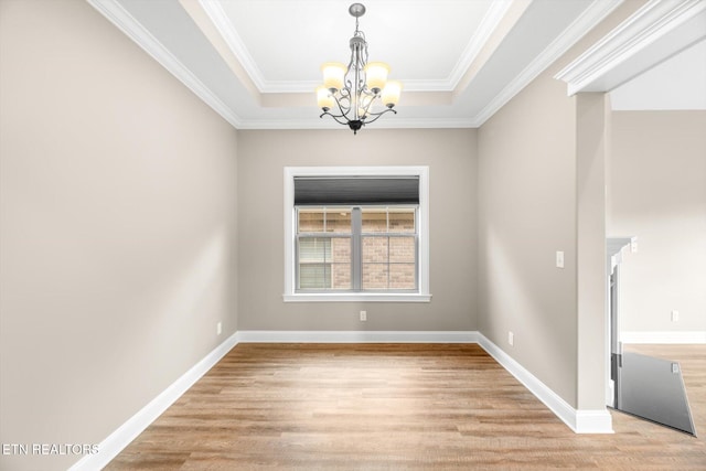spare room with a tray ceiling, ornamental molding, baseboards, a chandelier, and light wood finished floors