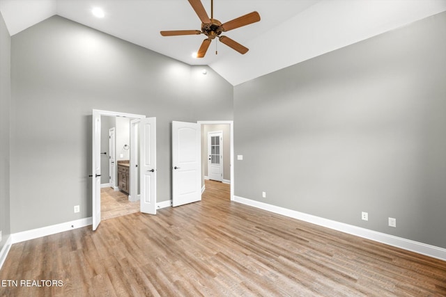 unfurnished bedroom with connected bathroom, high vaulted ceiling, baseboards, and light wood-type flooring