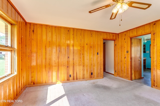 carpeted empty room featuring crown molding, ceiling fan, and wooden walls