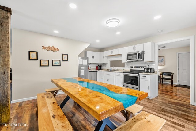 kitchen with light wood-type flooring, white cabinetry, backsplash, sink, and appliances with stainless steel finishes