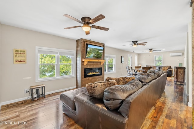 living area with baseboards, wood finished floors, ceiling fan, and a large fireplace