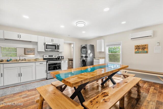 kitchen featuring light wood-type flooring, stacked washer and dryer, a wall mounted AC, stainless steel appliances, and sink