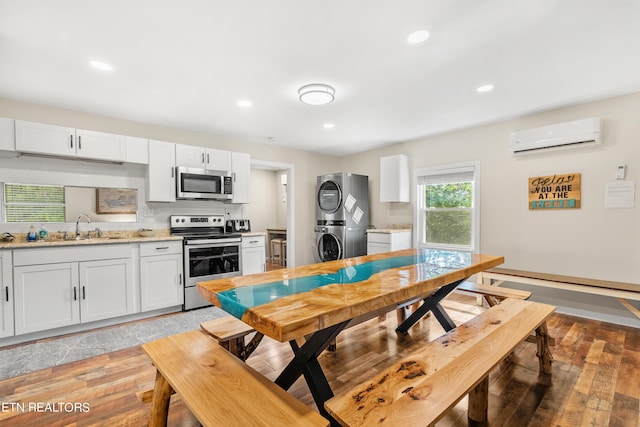 kitchen with stacked washer / drying machine, an AC wall unit, a sink, light wood-style flooring, and appliances with stainless steel finishes