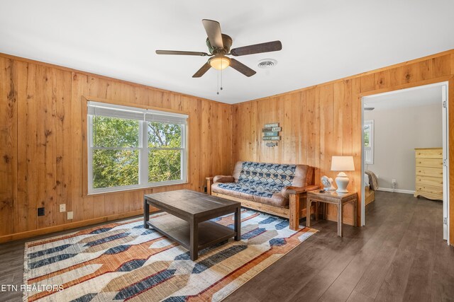 living room with dark wood-type flooring, ceiling fan, and wood walls