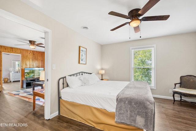 bedroom featuring visible vents, wooden walls, baseboards, ceiling fan, and dark wood-type flooring