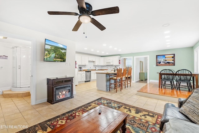 living room featuring baseboards, recessed lighting, a ceiling fan, a glass covered fireplace, and light tile patterned floors
