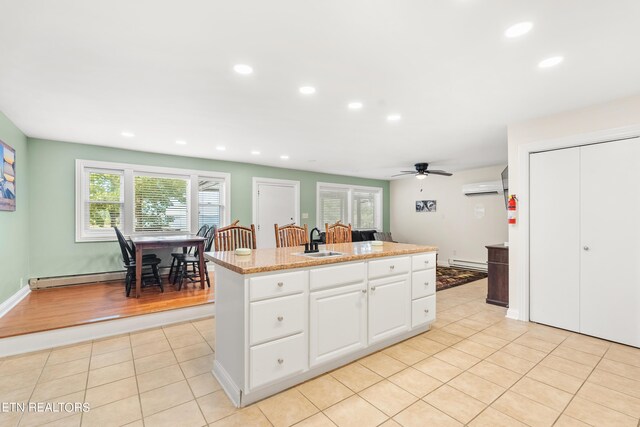 kitchen with a baseboard heating unit, ceiling fan, a wall mounted air conditioner, and white cabinetry